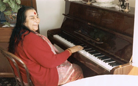 Shri Mataji Nirmala Devi in red cardigan playing an upright piano