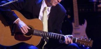 eric clapton, with suit, shirt and tie, playing acoustic guitar